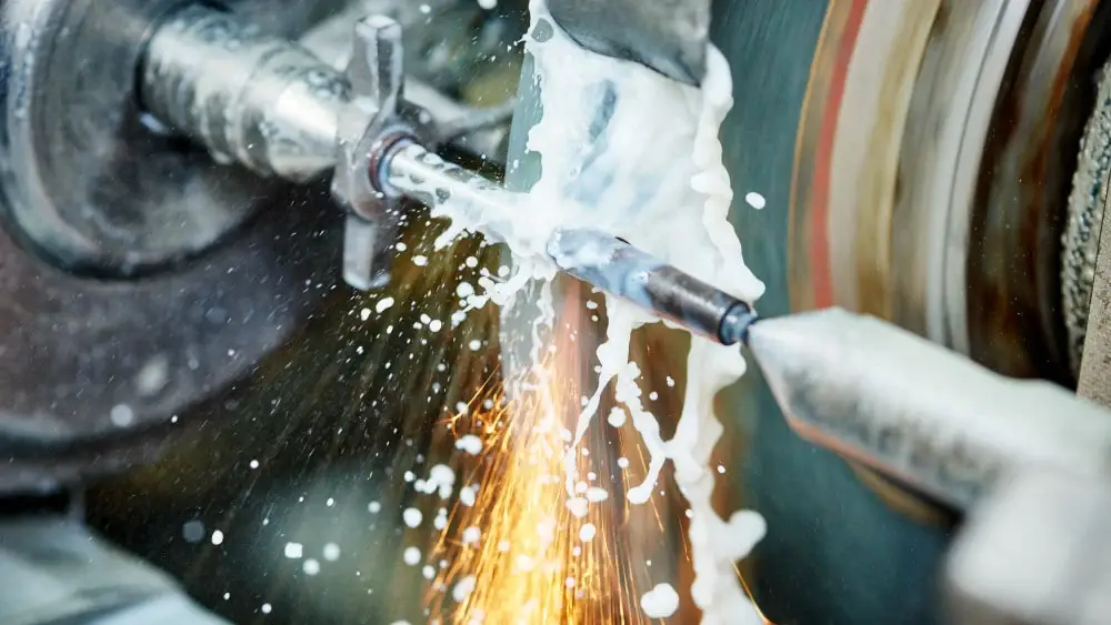 Close-up of cylindrical grinding process showing the fixed nozzle delivering grinding fluid.