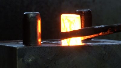 A heated blank just prior to being placed into dies in a mechanical forging press.