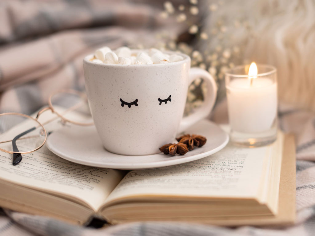 Glasses, book, hot drink, and candle set up in a home learning environment