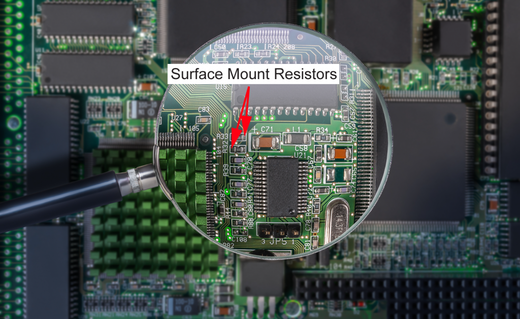 A magnifying glass focusing on surface mount resistors mounted on a PCB, along with other electronic components, illustrating how advanced resistor technology has become.