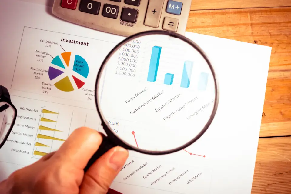 A hand holding a magnifying glass, focusing on a statistics bar graph.