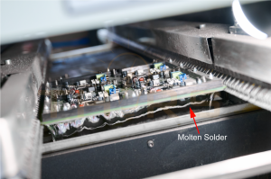 A PCBA immersed in molten solder in the wave soldering method.